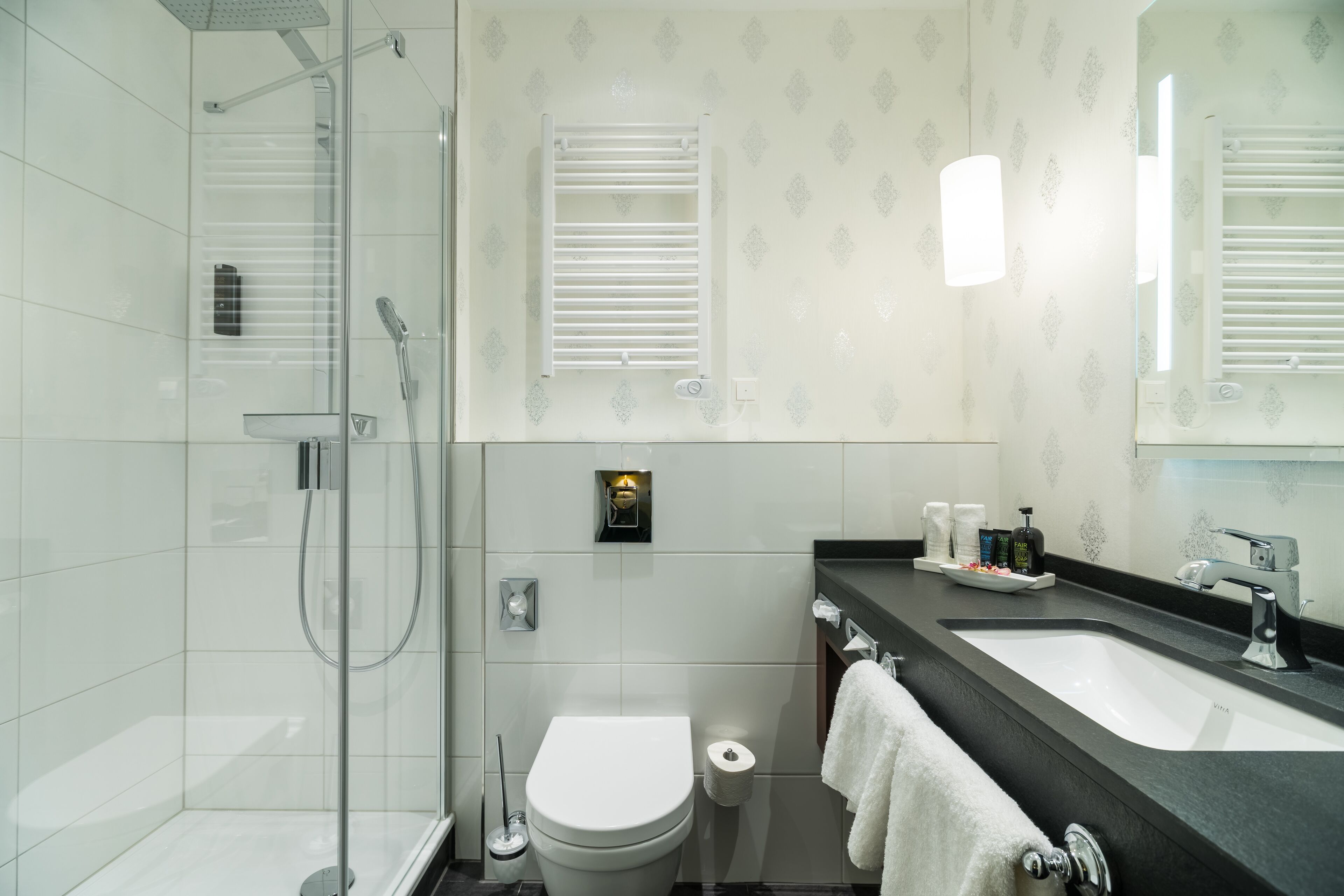 A modern bathroom with a glass shower enclosure, a white toilet, a sink with a black countertop, and a mirror above the sink.