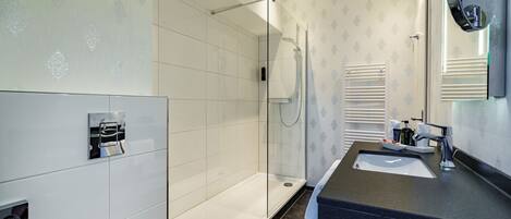 A modern bathroom with a glass-enclosed shower, a sink with a dark countertop, and a mirror.