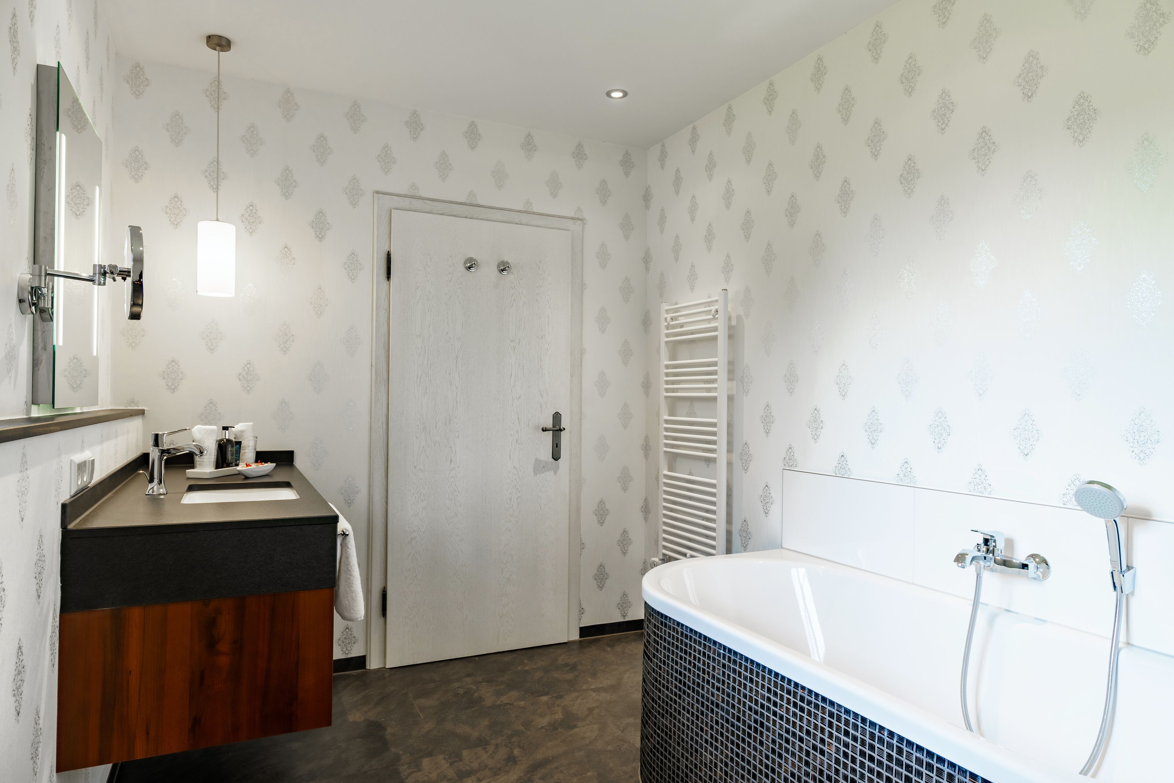 Ein Badezimmer mit einem Holzbadezimmer-Möbel, einem weißen Waschbecken, einer großen Badewanne und einem Handtuchhalter.