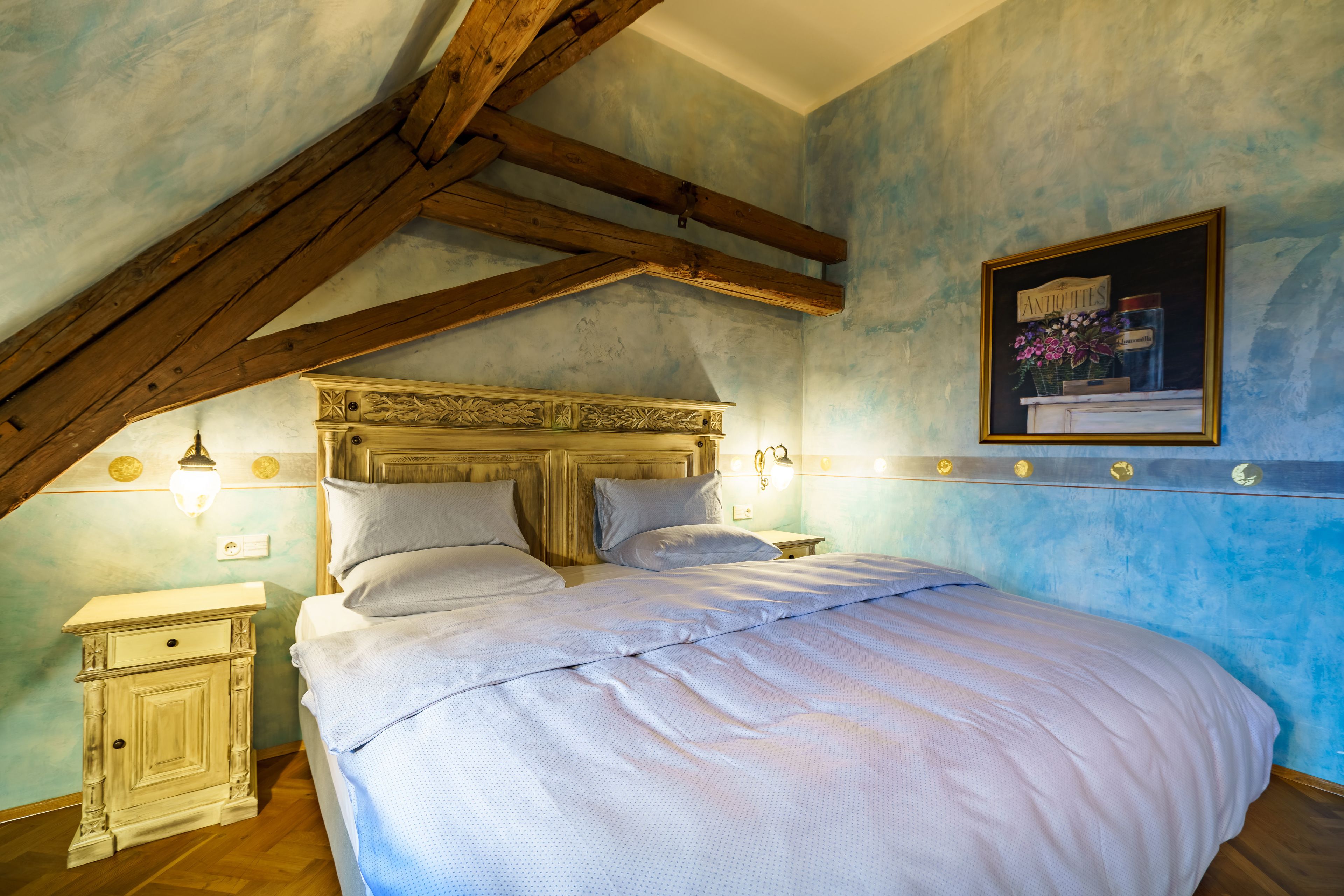 A bedroom with a wooden ceiling, a bed with white bedding, a nightstand, and a wall-mounted light fixture.