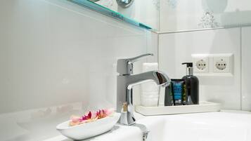 A modern bathroom with a white sink, a chrome faucet, and a glass bowl with flowers. There are two bottles of hair care products on the sink.