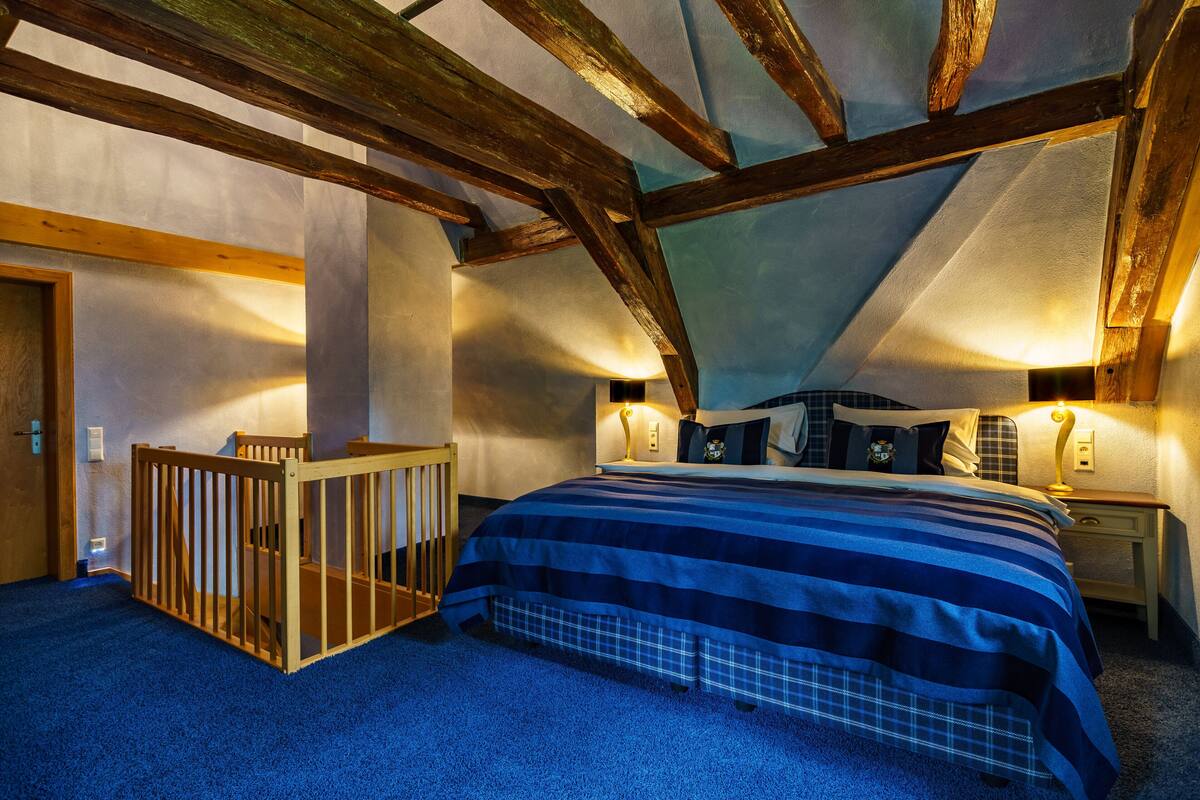 Een slaapkamer met een schuine plafond, houten balken, een ledikant, een bed met een gestreept beddegoed en bedlampen.