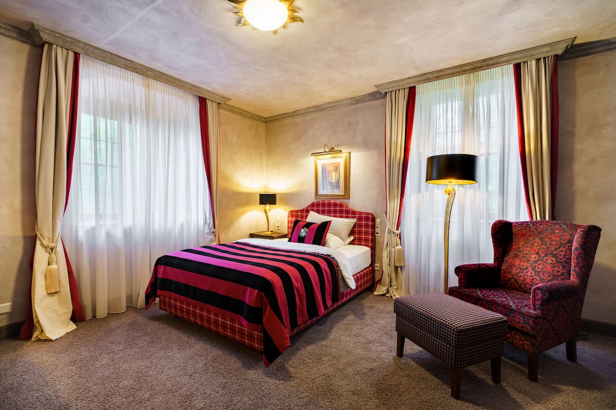 Een hotelkamer met een bed, een stoel, een lamp en gordijnen.