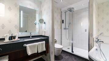 A modern bathroom with a large mirror, a sink, a toilet, and a shower area.