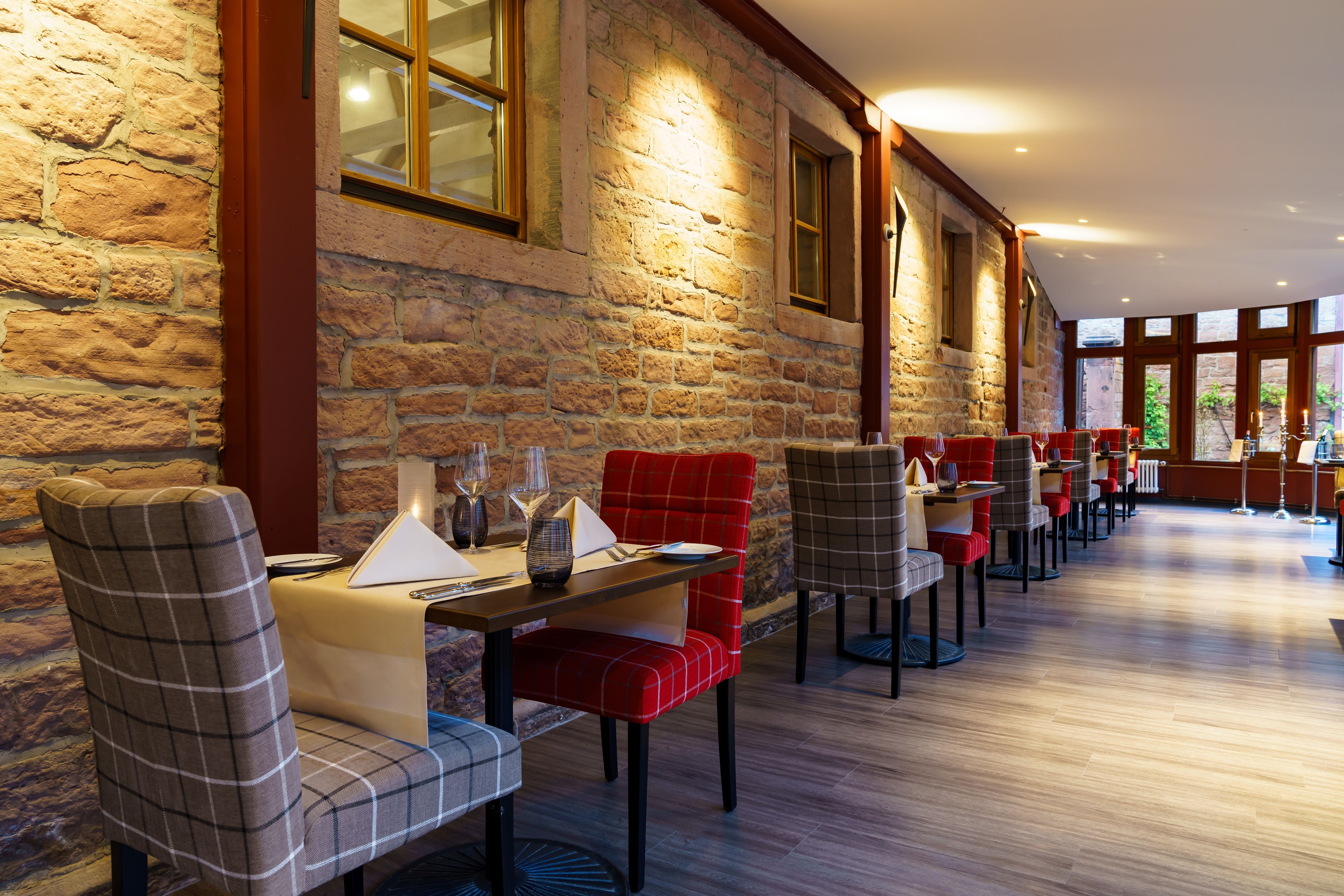 A restaurant with a stone wall and wooden beams, featuring red and grey checkered chairs and tables.