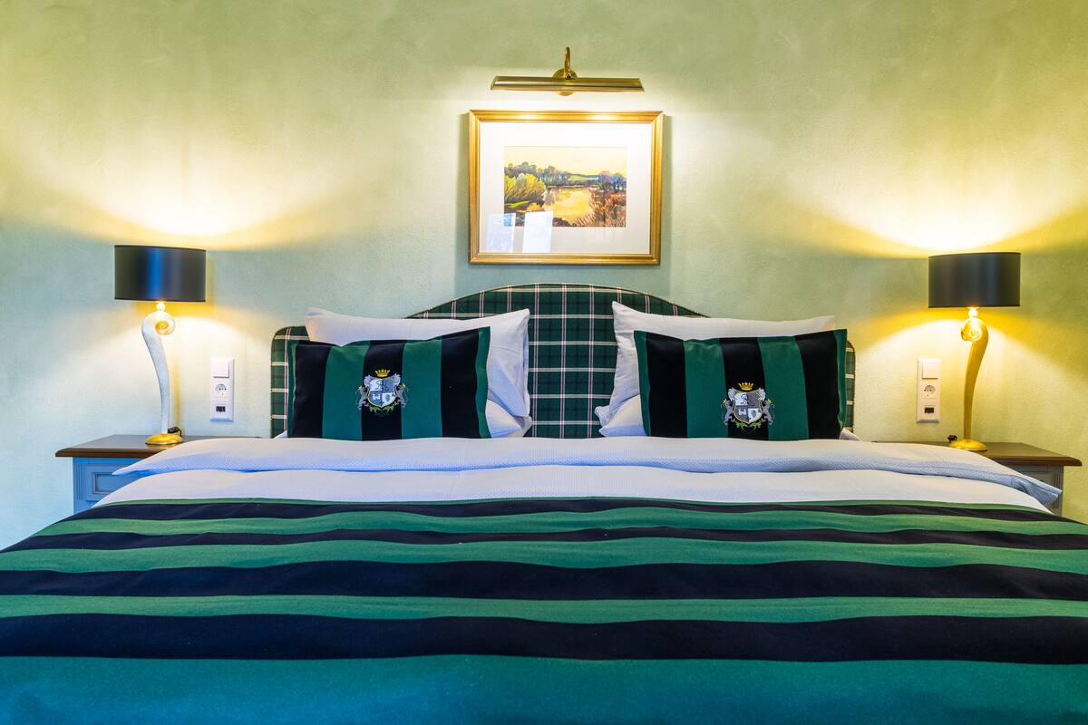 Een net opgemaakt bed met streepjesbeddengoed, twee bedlampjes en een ingelijst beeld aan de muur.