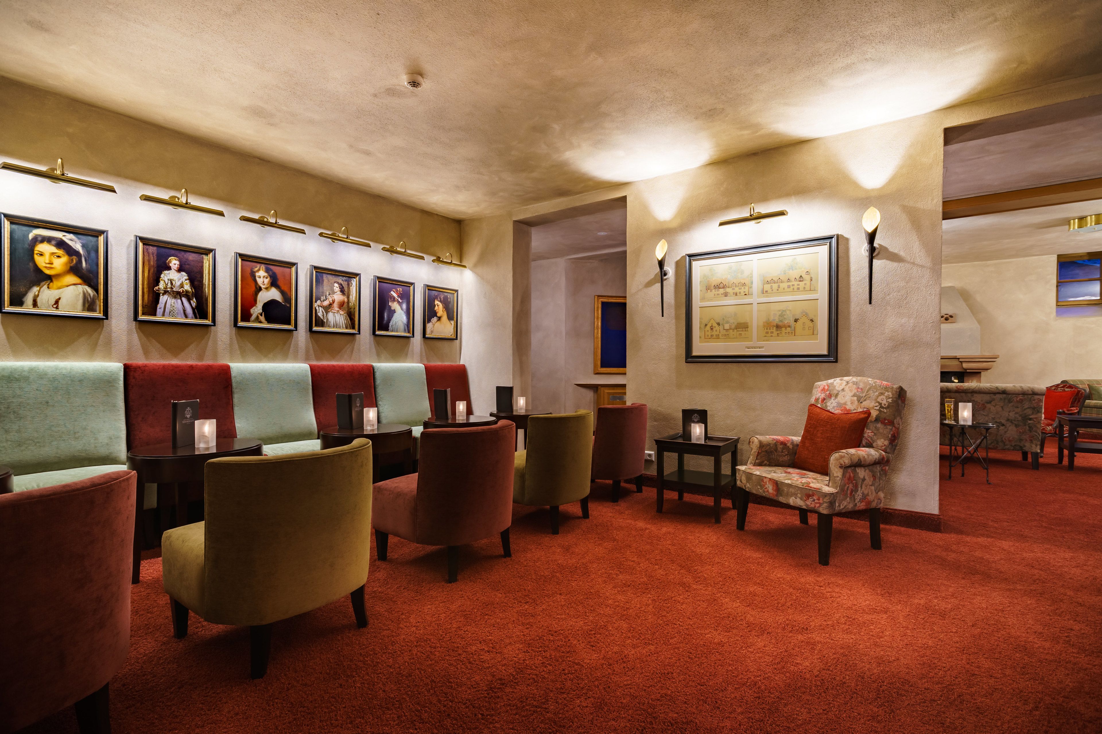A lobby with a red carpet, multiple seating areas with armchairs and sofas, framed artwork on the walls, and a fireplace.