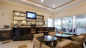 A bar area with a television, shelves of bottles, and a seating arrangement with tables and chairs. - Interclass Florianópolis (Florianópolis)