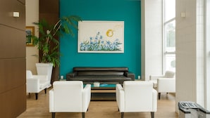 A modern lobby with a teal accent wall, a black leather sofa, white armchairs, and a large potted plant. - Interclass Florianópolis (Florianópolis)
