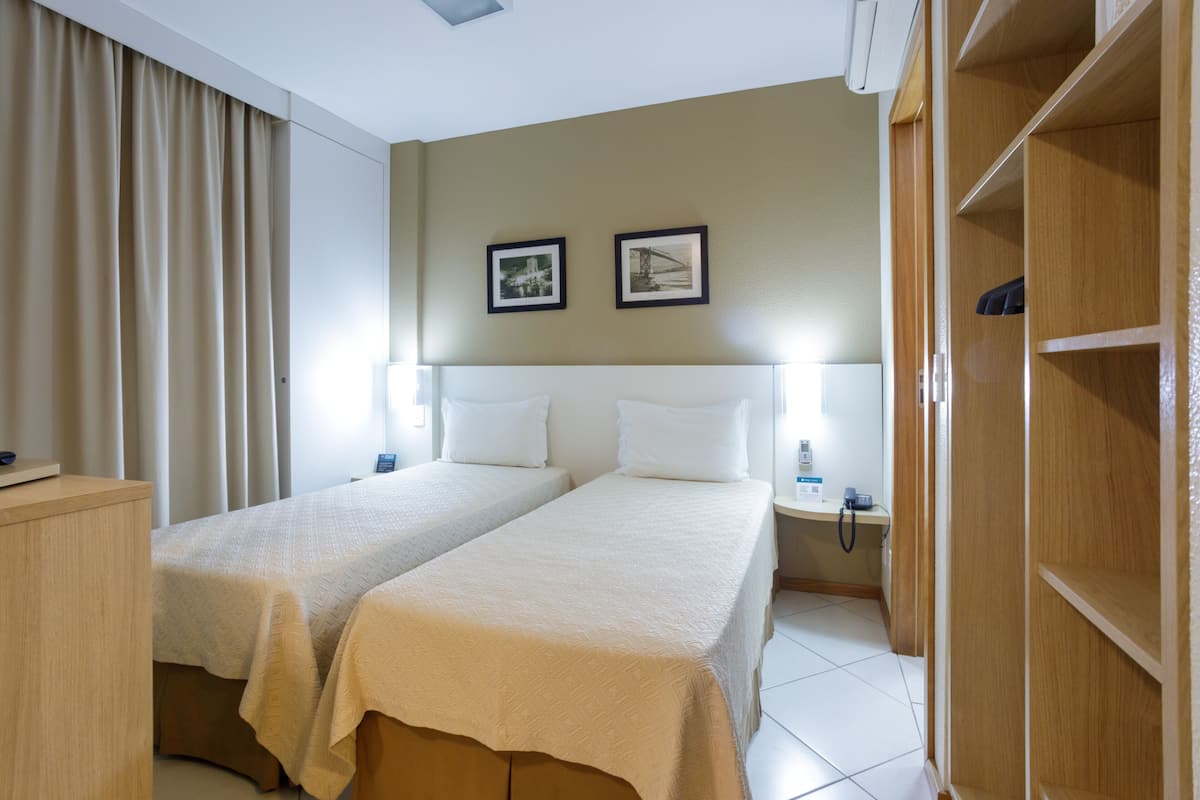 A hotel room with two beds, a wooden wardrobe, a nightstand with a phone, and two framed pictures on the wall.