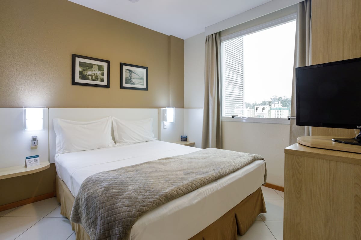 A hotel room with a bed, a TV on a wooden stand, and two framed pictures on the wall.