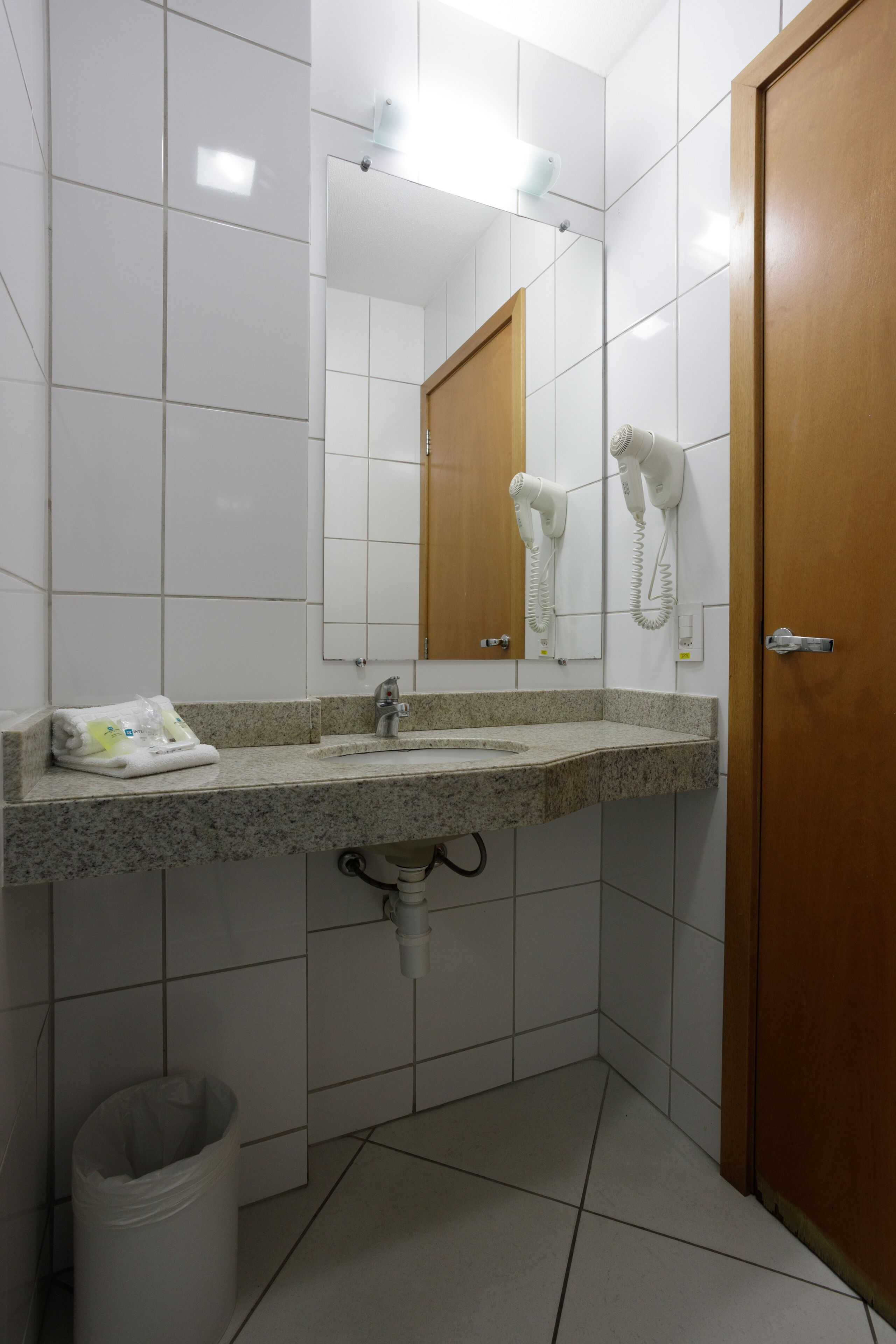 A bathroom with a granite countertop sink, a mirror, a hairdryer, and a trash can.
