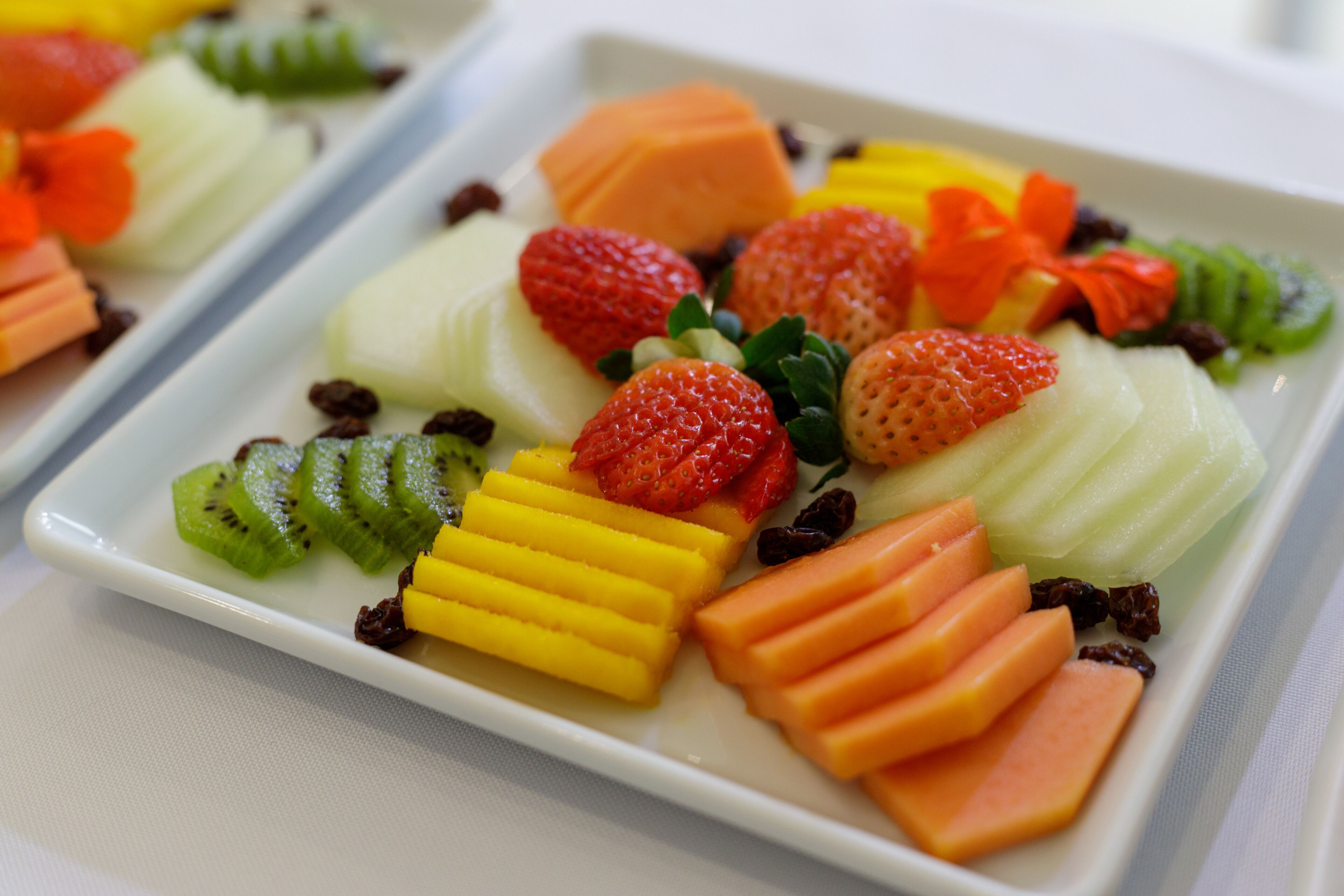 A white rectangular plate with various fruits and vegetables, including sliced kiwi, strawberries, and carrots.