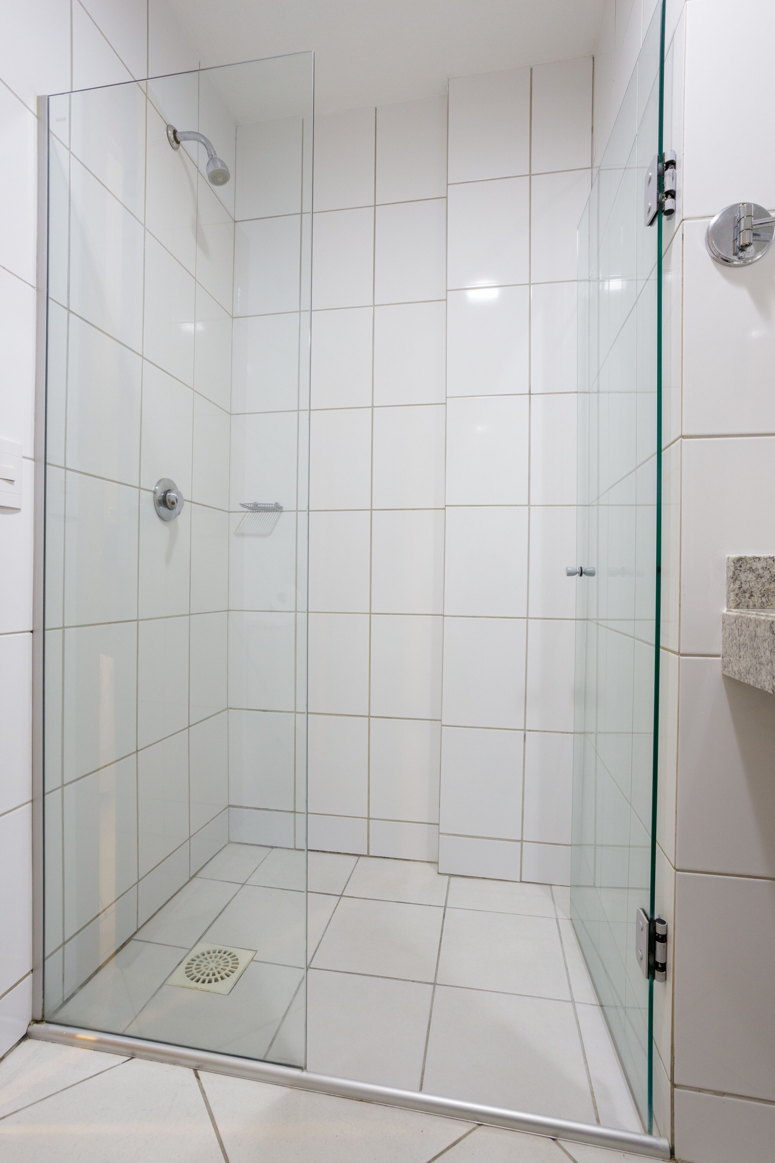 A glass-enclosed shower stall with white tiles and a metal showerhead.