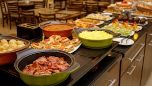 A buffet with various food items including potatoes, ham, and a green dish with yellow food. - Interclass Florianópolis (Florianópolis)