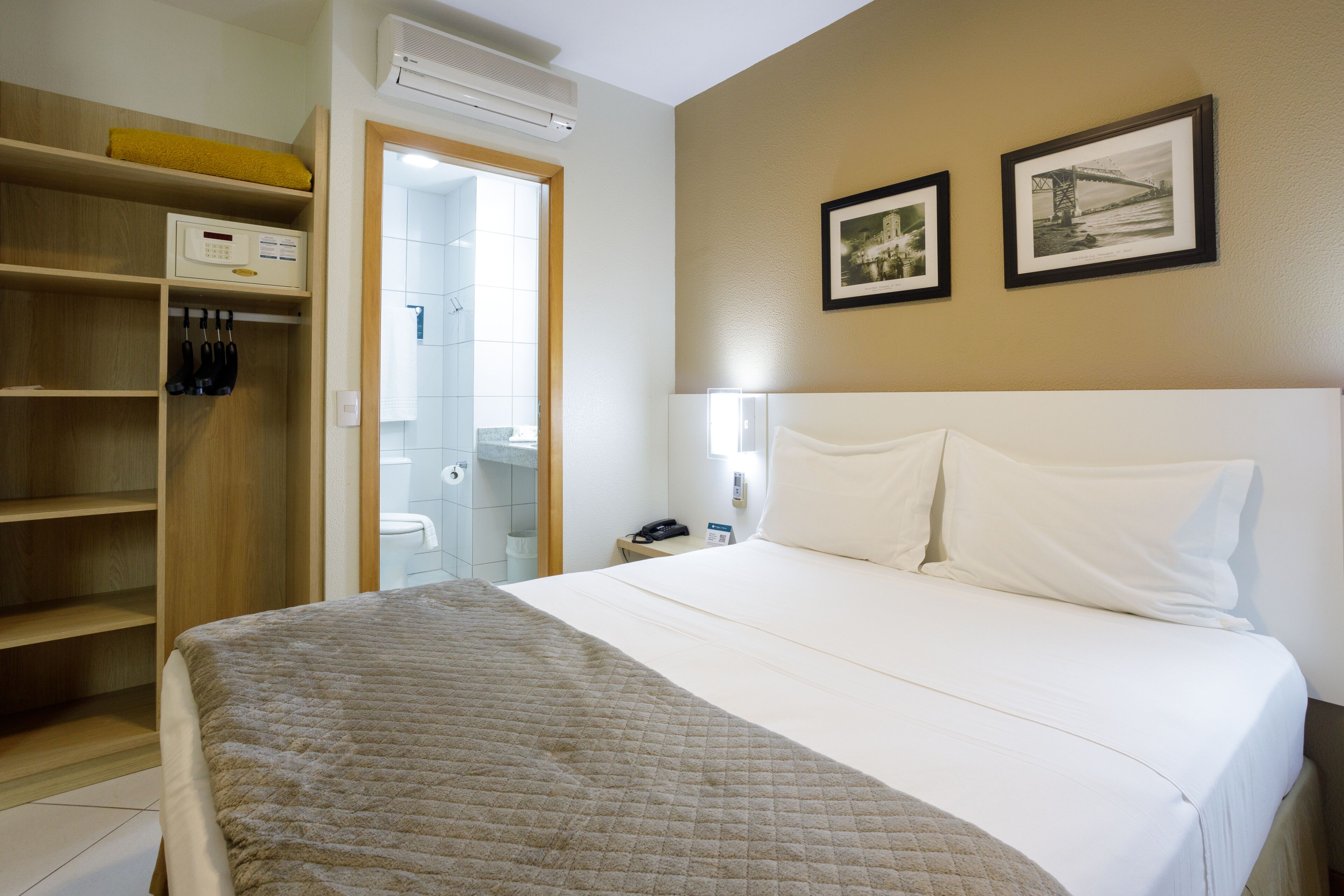 Una camera d'albergo con un letto, un armadio, un bagno e due quadri appesi al muro.