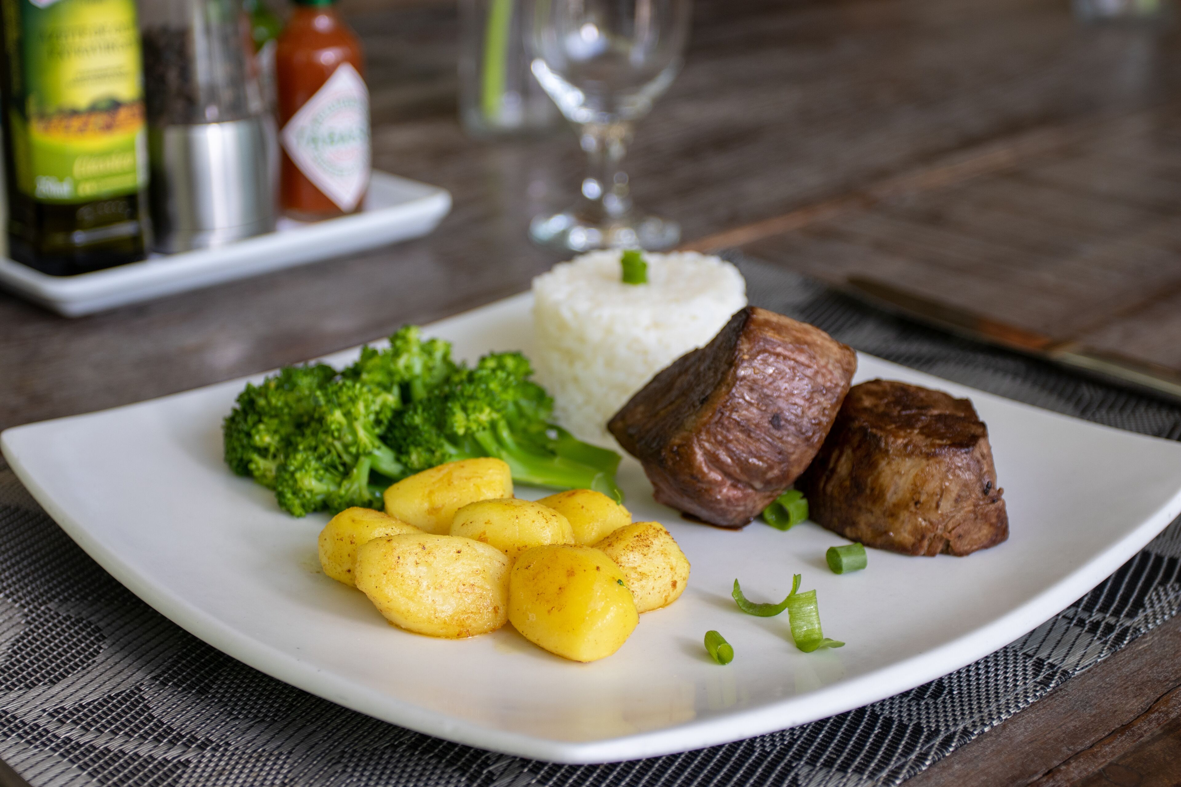 Un plato con arroz blanco, brócoli, patatas y dos trozos de carne sobre una mesa.