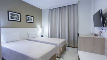 Habitación de hotel con dos camas, un escritorio, un televisor y una ventana con cortinas.