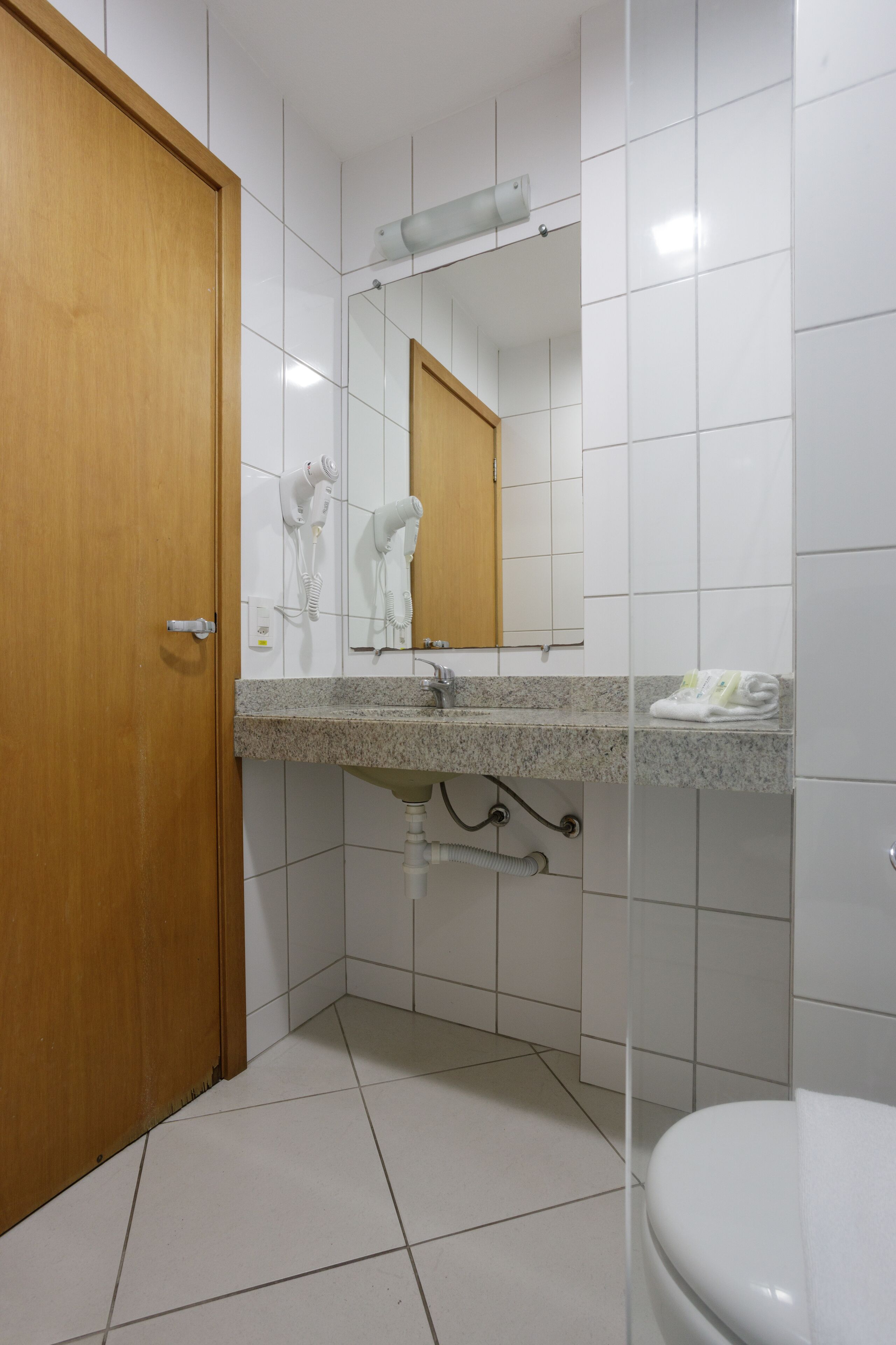 A bathroom with a wooden door, a sink with a mirror above it, and a toilet.