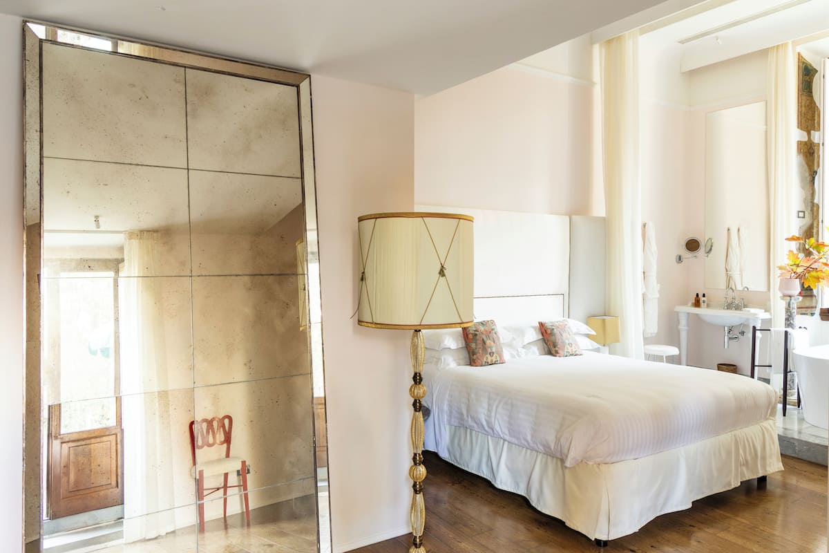 A spacious bedroom with a large bed, a bedside table, a mirror, and a bathroom with a sink and toilet.