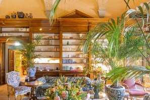 A library with bookshelves, a sofa, chairs, and potted plants. - Il Salviatino (Florence)
