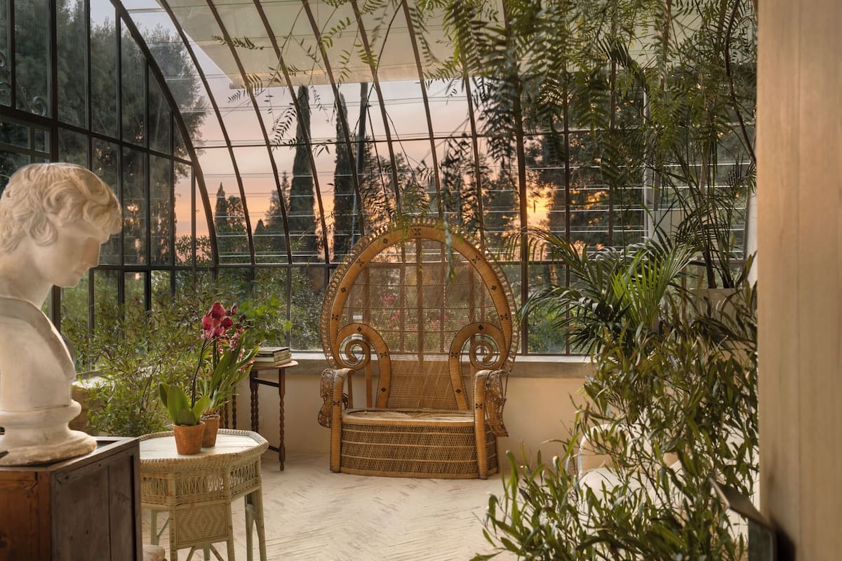 A conservatory with a wicker chair, a bust sculpture, and potted plants.