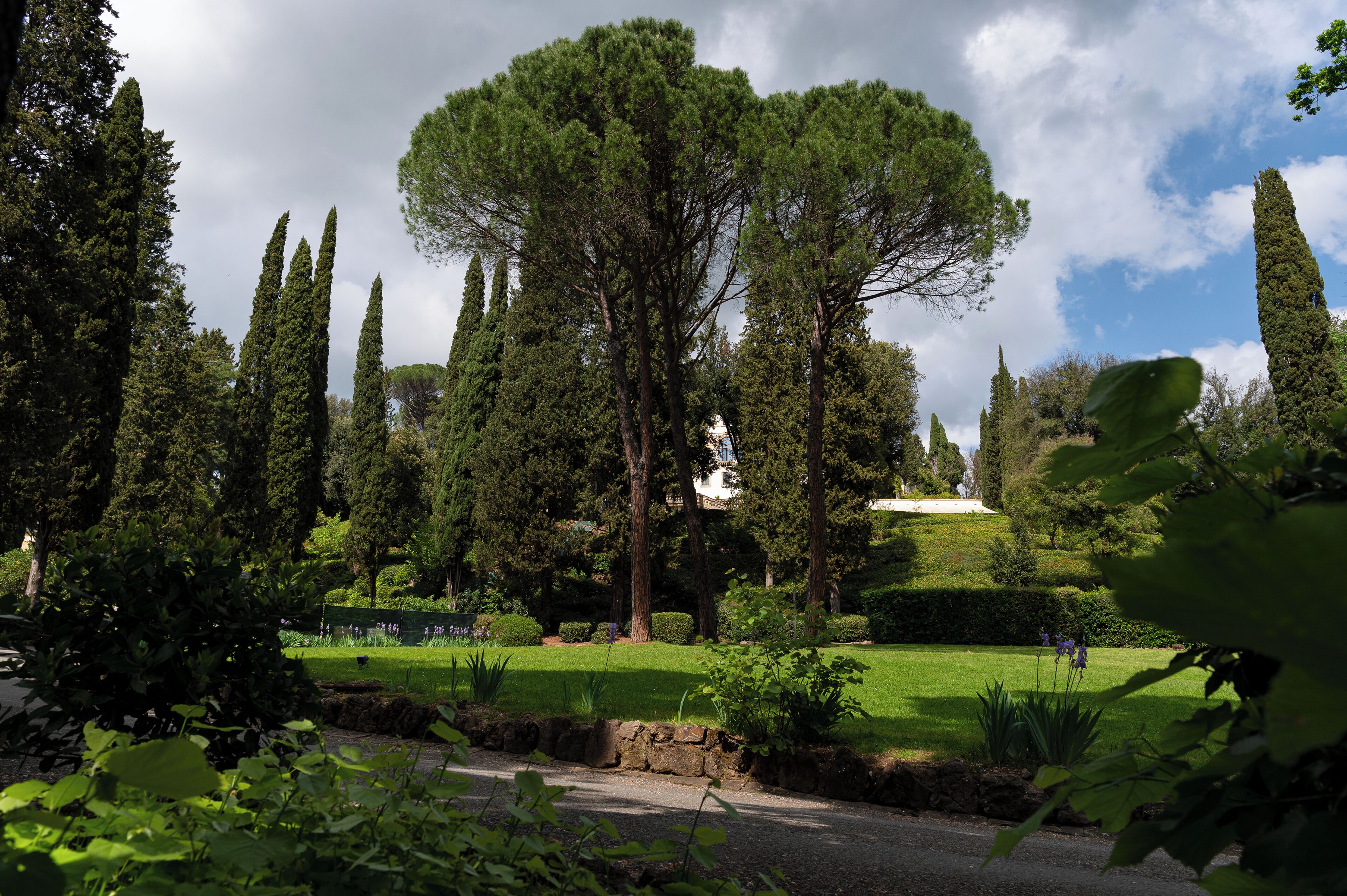 Un parque con una estatua, árboles altos y césped cuidado.