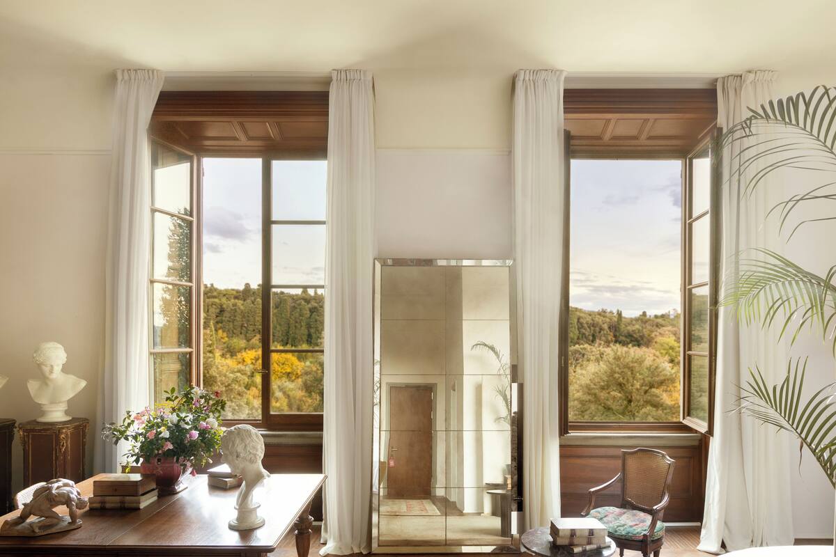 A room with large windows, a wooden table with decorative items, and a view of trees and hills.