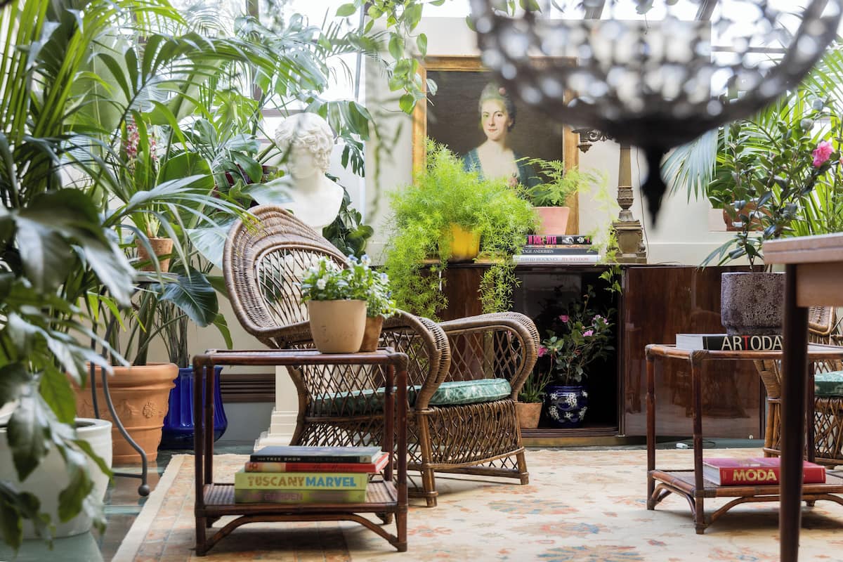 A cozy room with wicker furniture, potted plants, and books.