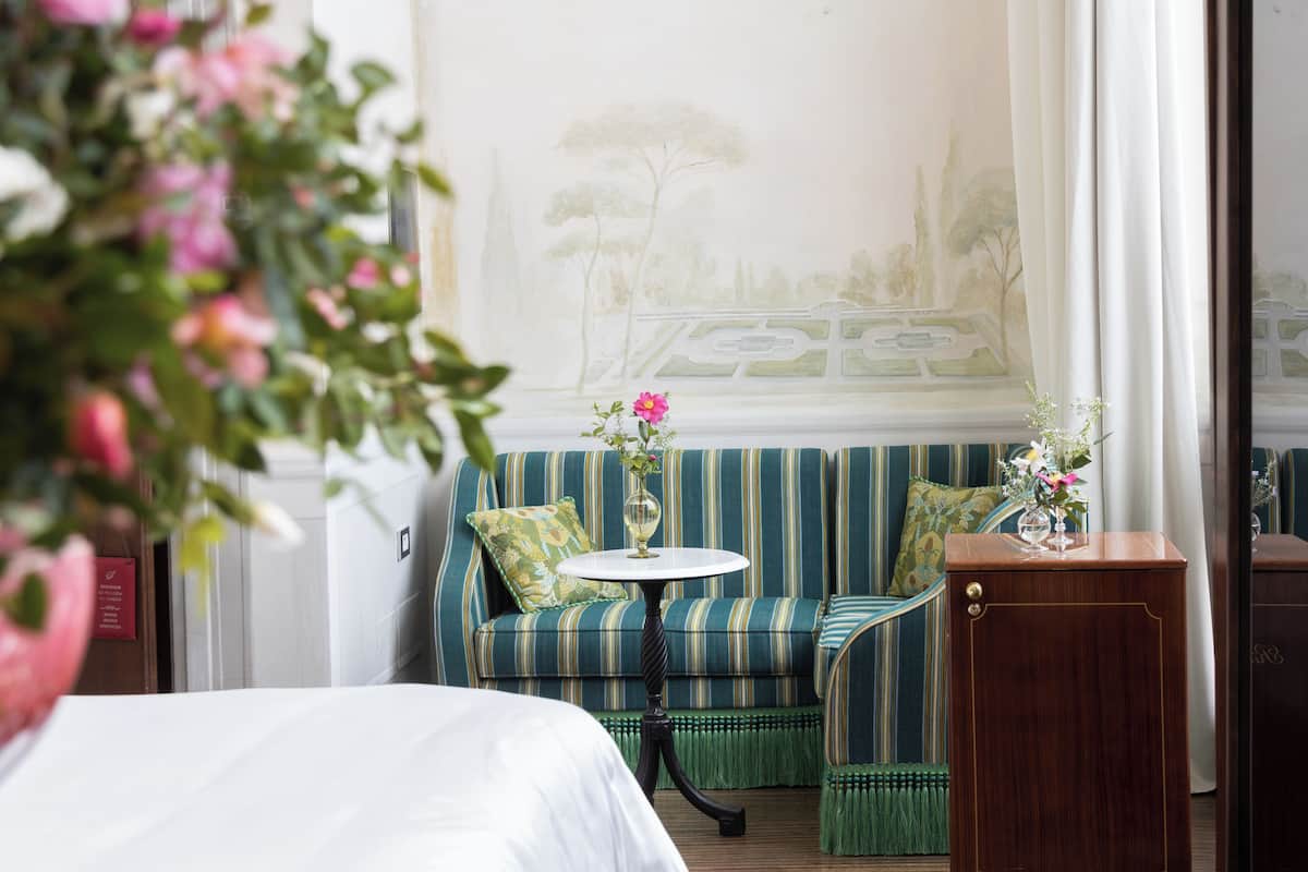 A room with a bed, a striped sofa, a small table with a vase, and a cabinet.