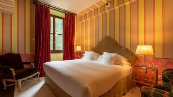 Ein Hotelzimmer mit einem großen Bett, zwei Nachttischlampen, einem Sessel und einem Fenster mit roten Vorhängen.