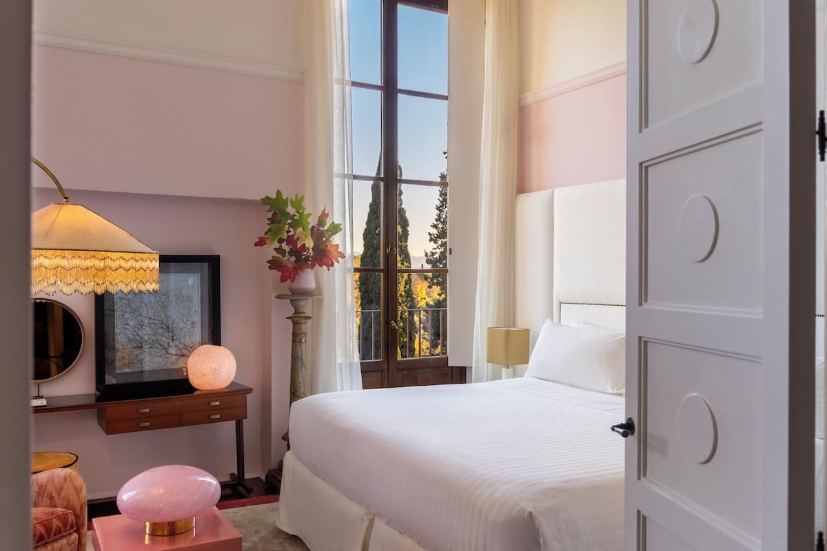 A bedroom with a large bed, a bedside table, a lamp, a decorative globe, and a window with a view of trees.