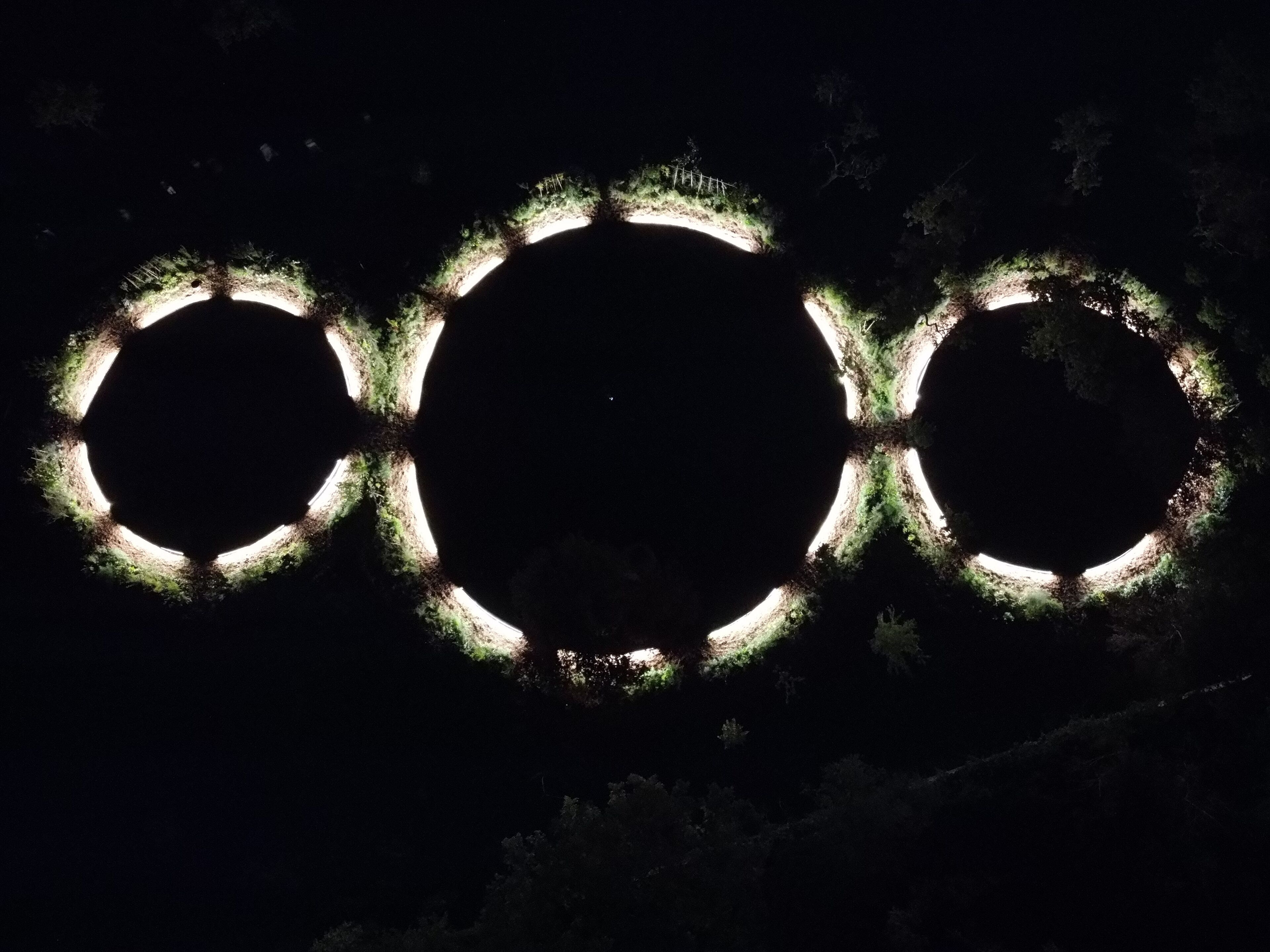Ein dunkler Himmel mit drei beleuchteten Ringen, die an die Olympischen Ringe erinnern.