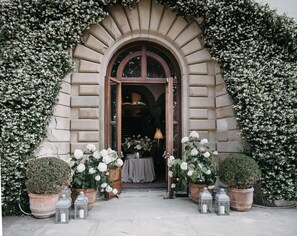 An entrance with a stone archway, potted plants, and a table with a lamp. - Il Salviatino (Florence)