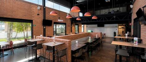 Un interior de restaurante moderno con paredes de ladrillo, grandes ventanales y varias zonas de estar.