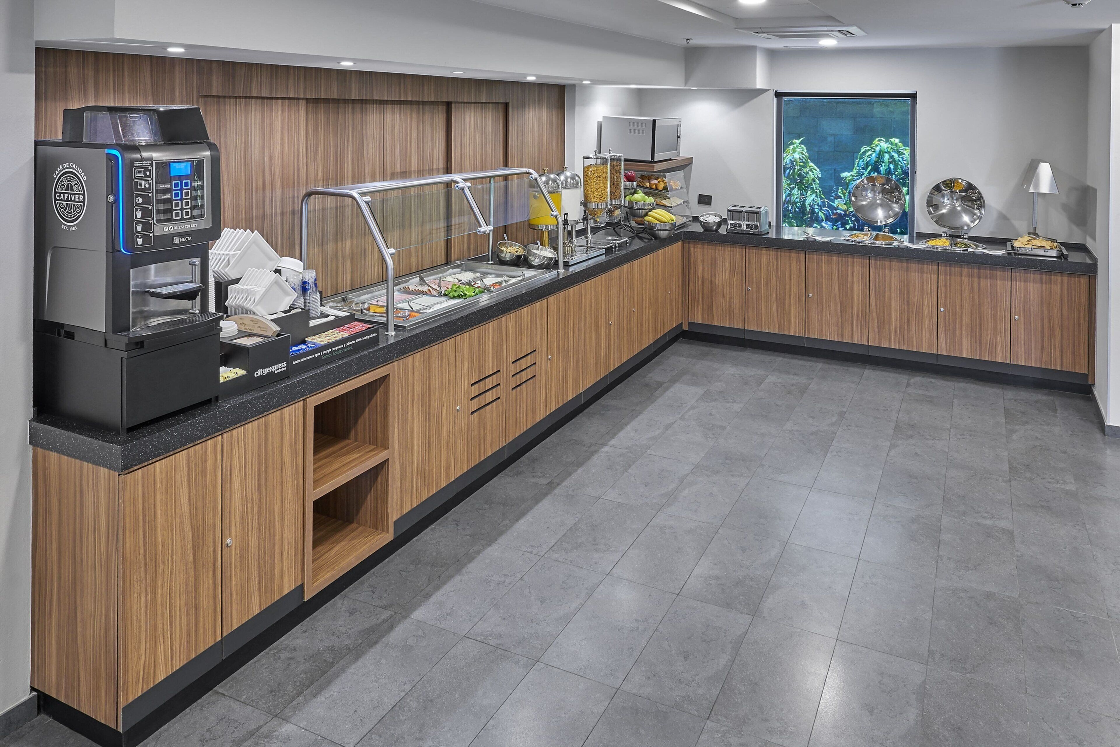 Un espace buffet comprenant une machine à café, des distributeurs de nourriture et un comptoir où sont présentés divers aliments.