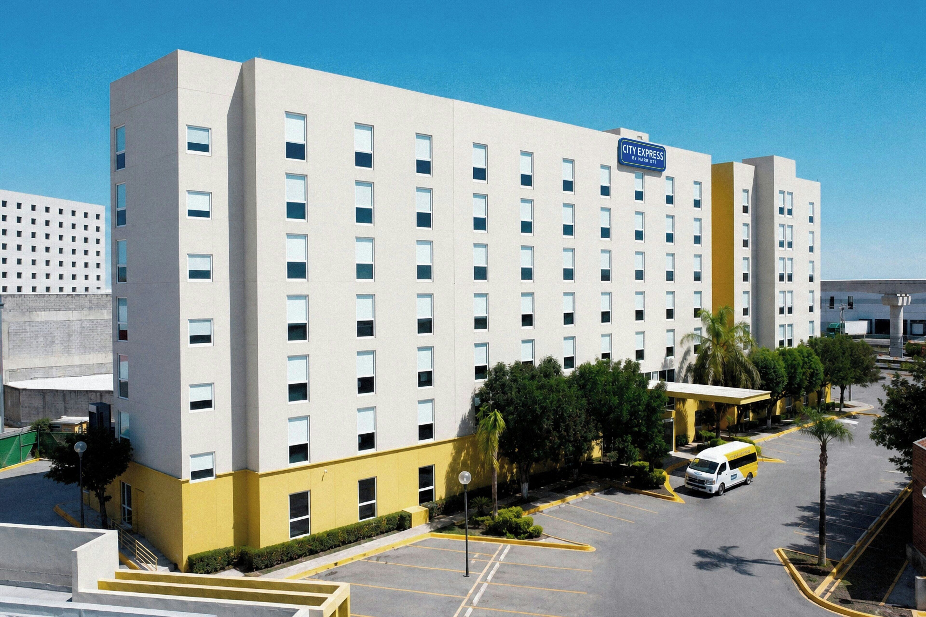 A multi-story hotel with a City Express sign, parking lot, and surrounding greenery.