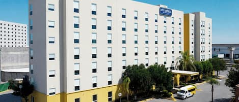 A multi-story hotel with a City Express sign, parking lot, and surrounding greenery.