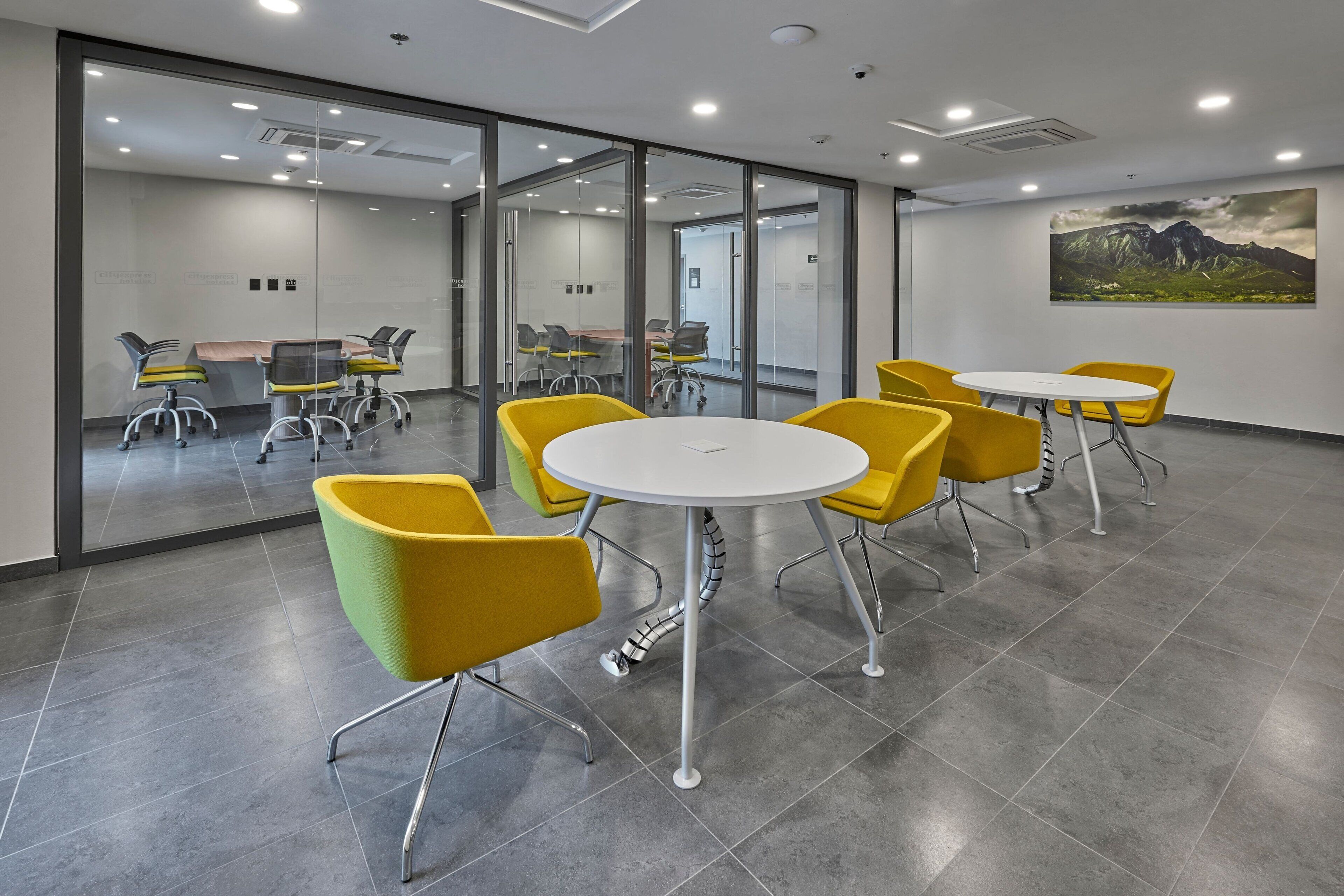 A modern conference room with glass walls, yellow chairs, and a white table.