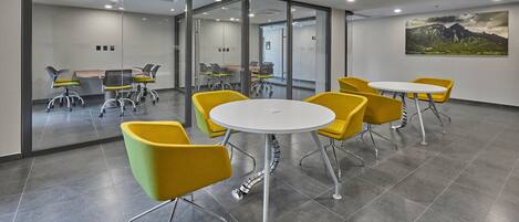 A modern conference room with glass walls, yellow chairs, and a white table.