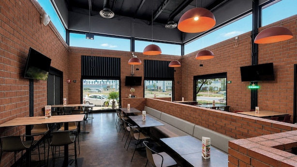 Un restaurante con paredes de ladrillo, ventanas amplias e iluminación colgante.