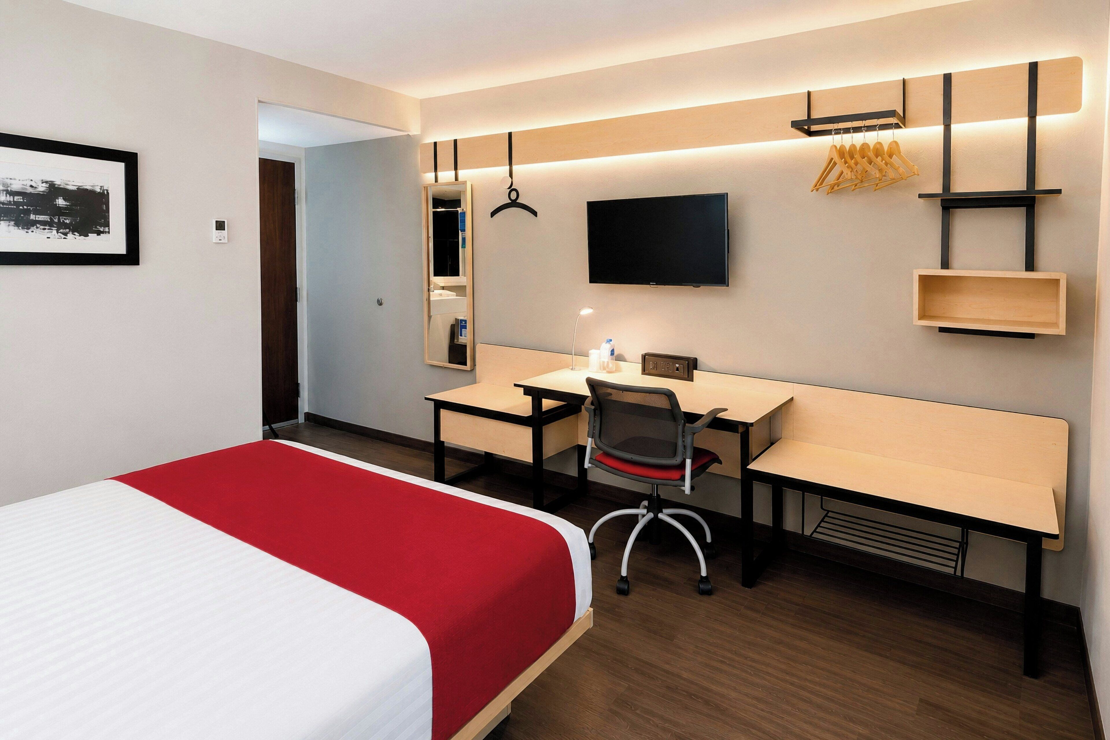 Een hotelkamer met een bed, bureau, stoel, televisie en een spiegel.