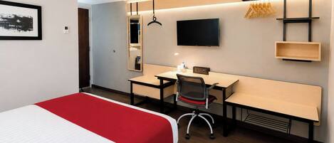 Een hotelkamer met een bed, bureau, stoel, televisie en een spiegel.