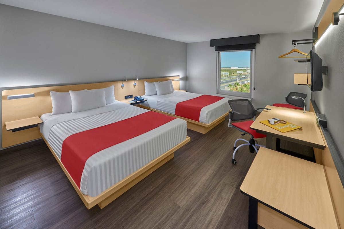 Habitación de hotel con dos camas, un escritorio, una silla, un televisor y ventana con vistas.