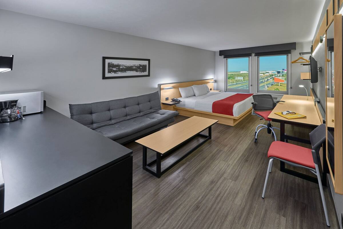 Habitación de hotel moderna con cama, sofá, escritorio y vistas a la ciudad.