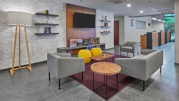 A modern lobby with grey armchairs, a round wooden table, and a large floor lamp.