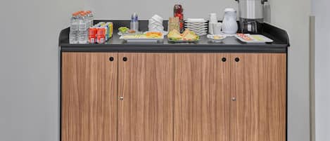 A hotel buffet counter with a variety of food items, beverages, and a coffee maker.