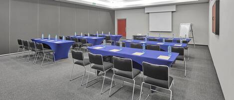 Un salón de conferencias con varias mesas y sillas, equipado con botellas de agua y tarjetas de identificación.