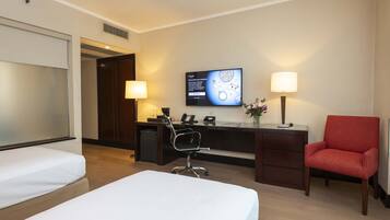 A hotel room with a bed, desk, chair, and a TV on the wall.