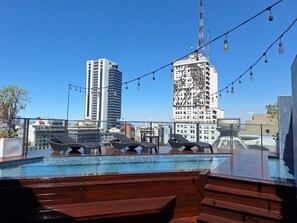 Ein Pool auf dem Dach mit Liegestühlen und Blick auf Stadtgebäude.